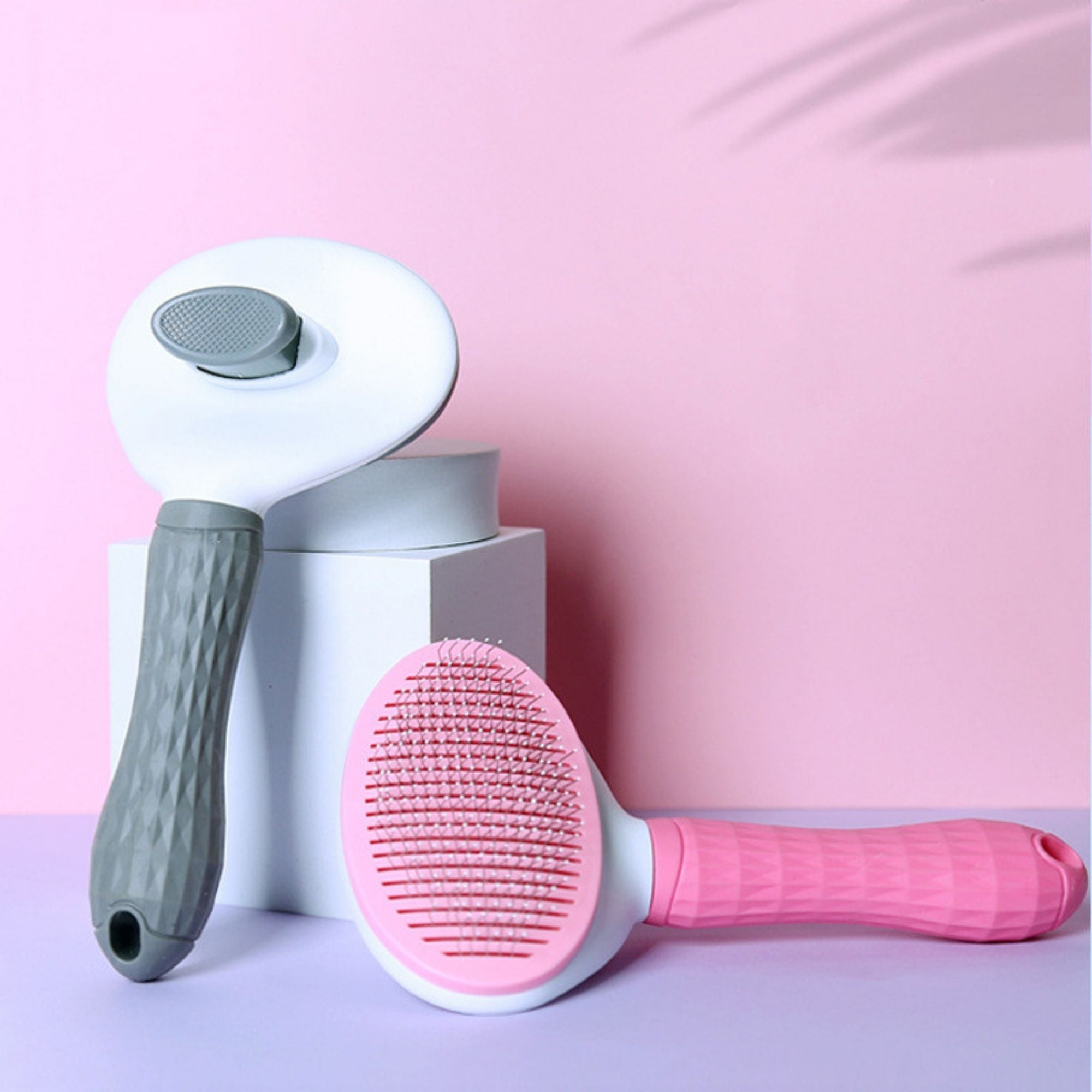 Gray and pink oval pet slicker brushes displayed on a pink background.
